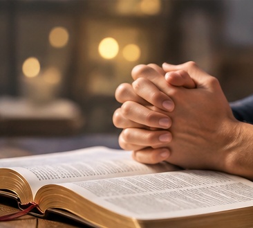 Hands folded in prayer over an open Bible